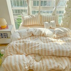 an unmade bed with striped sheets and pillows in front of a large window on a wooden floor