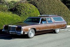 a brown station wagon parked on the side of the road next to bushes and trees