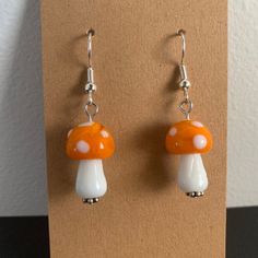 a pair of orange and white mushroom earrings on a brown card with silver earwires