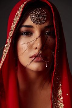 a woman wearing a red veil with gold jewelry on her face and nose is posing for the camera