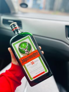 a person holding up a bottle of liquor in their hand next to a steering wheel