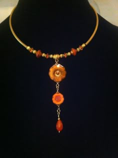 a necklace with orange beads and an orange flower hanging from it's center, on a black mannequin