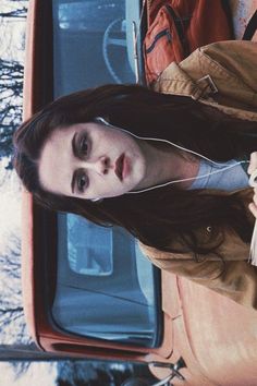 a woman standing in front of a car with her headphones hanging out the window