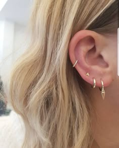 a woman with blonde hair is wearing gold ear climbrs and an earring that has two small stars on it