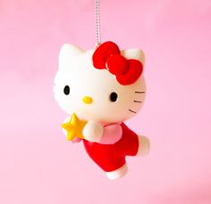 a hello kitty ornament hanging from a string on a pink background with a yellow star