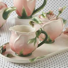 three pink roses are sitting on a white plate with matching cups and saucers in the shape of teapots