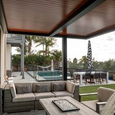 an outdoor living area with couches and tables next to a swimming pool in the background