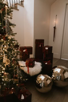 a christmas tree with presents under it in front of a staircase and some shiny balls on the floor