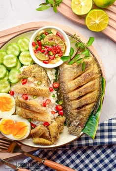 two fish on a plate with lemons, tomatoes and cucumbers next to it