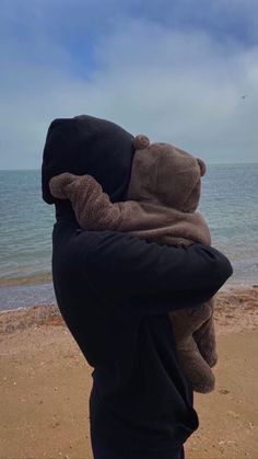 a person holding a teddy bear in their arms on the beach by the water's edge