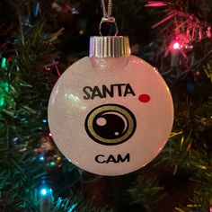 a glass ornament hanging from a christmas tree with the word santa cam on it