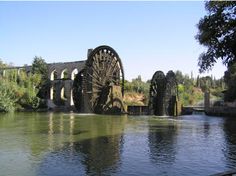 an old water wheel sitting on the side of a river