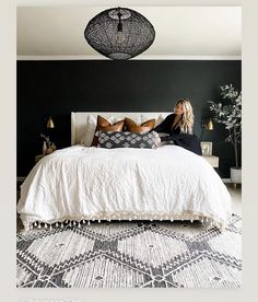 a woman sitting on top of a bed next to a black and white rug in a bedroom