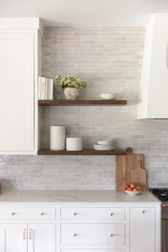 a kitchen with white cabinets and open shelving above the countertop, along with a bowl of fruit