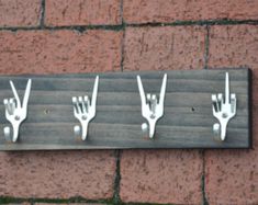 four forks are attached to a wooden plaque on the wall, with hooks hanging from it's sides