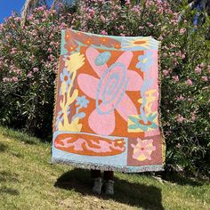 a woman standing in front of a bush holding up a colorfully colored blanket that has flowers on it