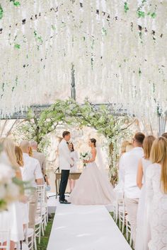 a bride and groom standing at the end of their wedding ceremony under an archway decorated with white flowers