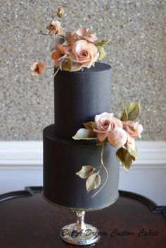 a three tiered black cake with pink flowers on top