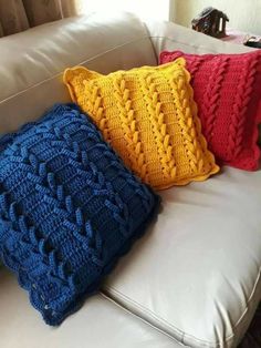 three knitted pillows sitting on top of a white leather couch next to each other