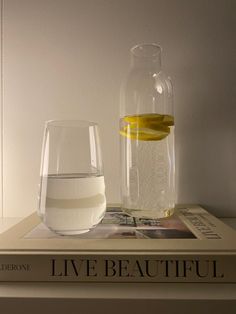 a glass and bottle sitting on top of a book next to a vase filled with water