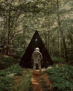 a robot standing in the middle of a forest next to a triangular shaped structure with trees around it