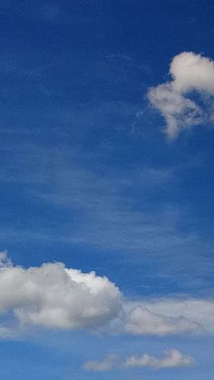 the airplane is flying high in the blue sky with white fluffy clouds on it's side