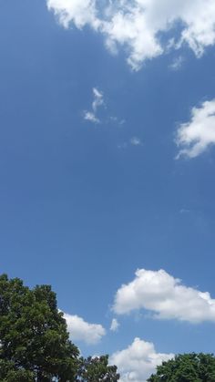 an airplane is flying high in the sky above some trees and grass on a sunny day