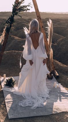 the back of a woman in a white dress standing on a blanket with feathers hanging from it