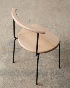 a wooden table with two black legs and a curved top sitting on concrete flooring