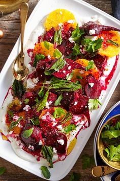 a white platter filled with food next to a bowl of salad and two gold spoons