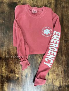 a red sweatshirt with the words emergency on it and a shamrock in white letters is laying on a wooden floor