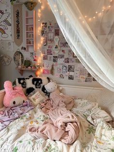 two stuffed animals laying on top of a bed in a room with white curtains and lights