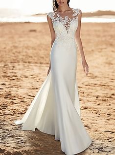 a woman is standing on the beach wearing a wedding dress with an open back and lace detailing