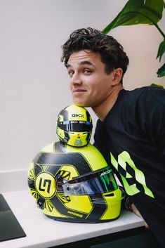 a man sitting next to a yellow motorcycle helmet on top of a table in front of a plant