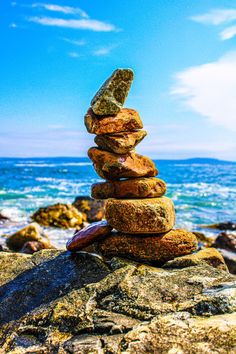 a stack of rocks sitting on top of a beach next to the ocean in front of a blue sky