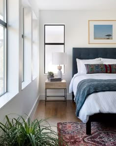 a bedroom with a bed, nightstands and plants on the side table in front of it