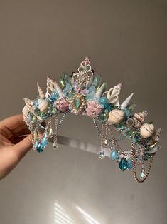 a hand is holding a tiara with seashells and pearls