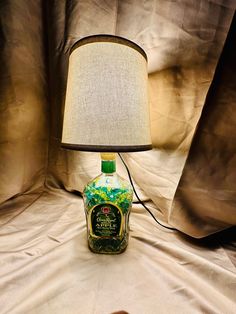 a lamp that is next to a bottle on a bed with a curtain in the background