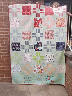 a woman is holding up a quilt on the porch