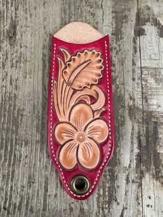 a leather case with flowers on it sitting on a wooden table next to a bottle opener