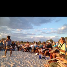 a group of people sitting on top of a sandy beach next to each other in front of a crowd