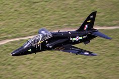 a fighter jet flying over a lush green field