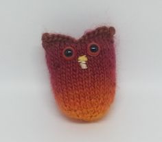 an orange and red knitted owl with big eyes on it's head, sitting in front of a white background