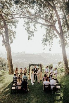 a group of people standing around each other in front of a tree filled field with chairs