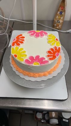 a decorated cake sitting on top of a metal tray next to a white plate with an orange, yellow and pink frosting