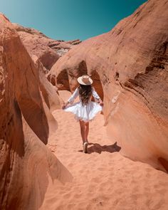 a woman in a white dress and hat walking through the desert