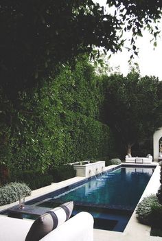 an outdoor swimming pool surrounded by greenery and white couches with pillows on it