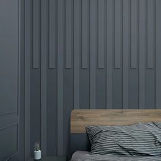 a bed sitting next to a gray wall with vertical striped sheets on top of it