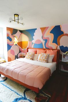 a large bed sitting in a bedroom next to a wall painted with colorful designs on it