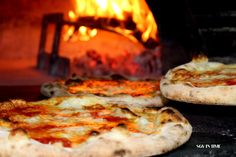 two pizzas sitting in front of an oven with fire coming from the oven door